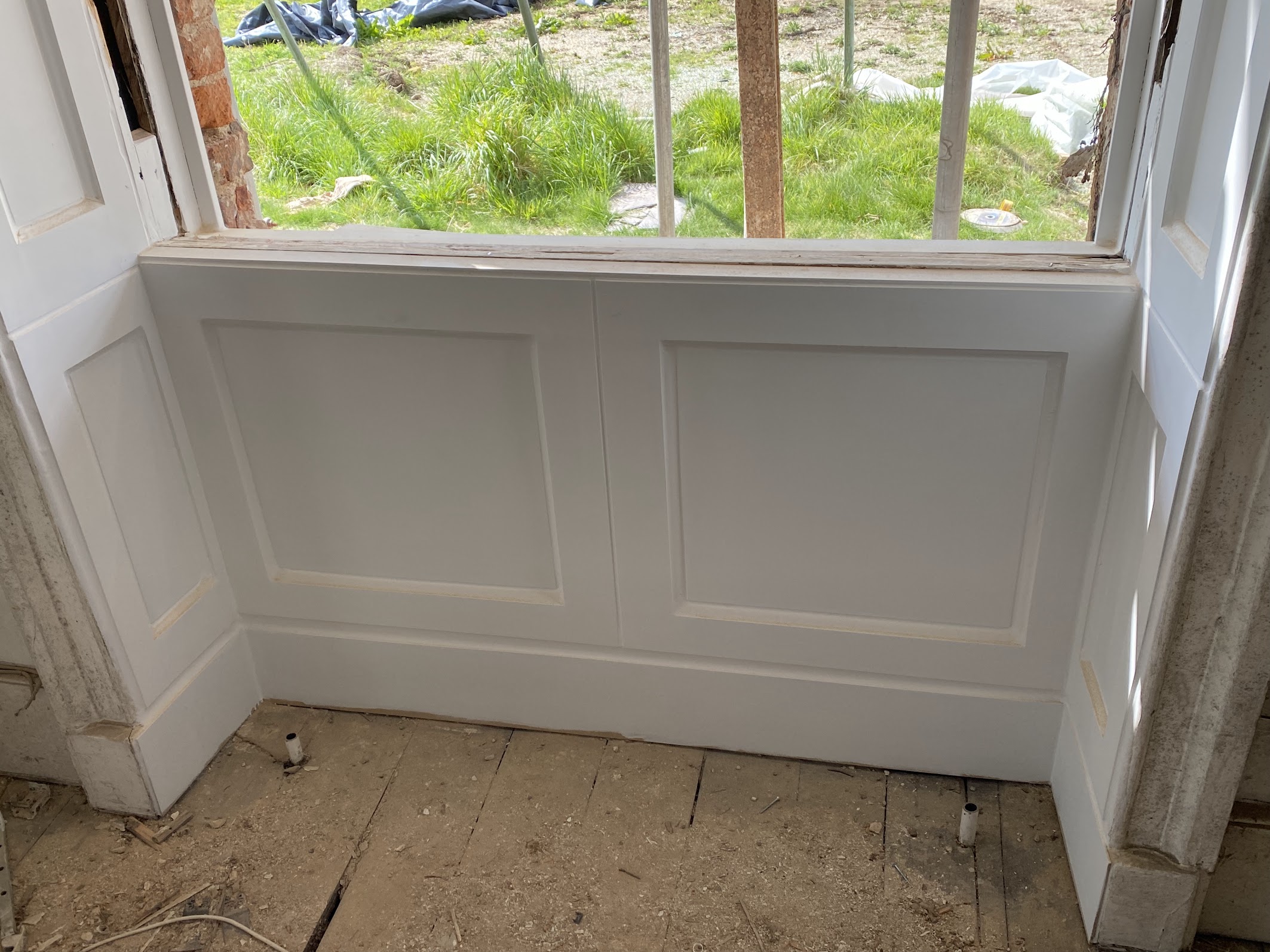 A white interior wooden panel is fitted below a window frame, with unfinished flooring and building materials visible, highlighting ongoing sash window repair in South London.