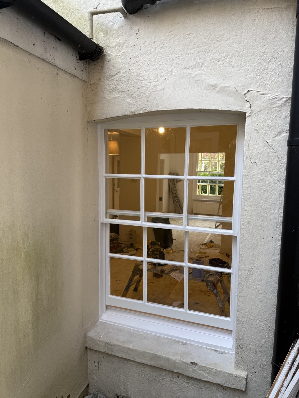 A white-framed window with grid panes set in a cream-coloured wall overlooks a room under renovation, tools and materials scattered on the floor—showcasing the need for expert Sash Window Repair South London.